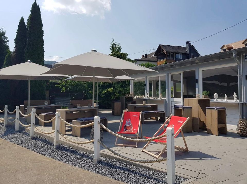Terrasse des Beachhouse an der Mosel: Sonnenschirme, Liegestühle, Seilgeländer, dahinter die Weinberge